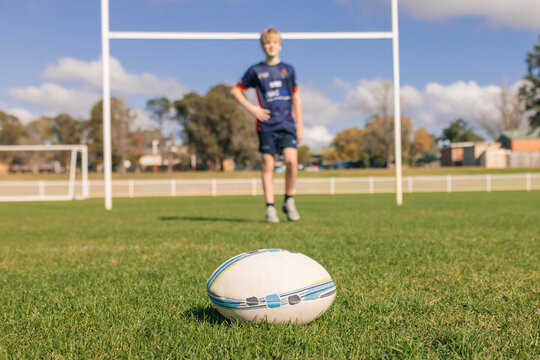 Rugby ball on field with player and goal posts in background