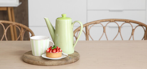Green teapot, cup and tasty cupcake on dining table in kitchen