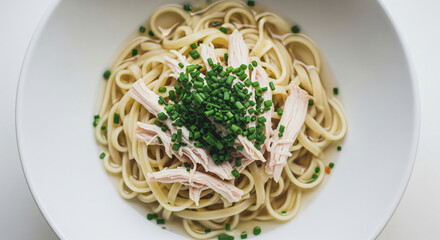 Creamy pasta swirl topped with tender shredded chicken and fresh green chives in a clean white bowl on a rustic wooden surface