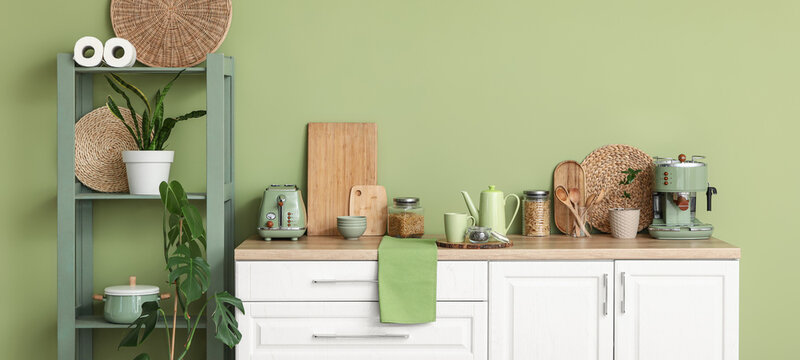 Interior of kitchen with teapot, jar of dry tea and cup on table near green wall