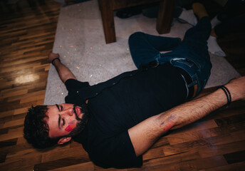 A man lies on the floor with a tired expression, lipstick marks on his face, reflecting a lively...