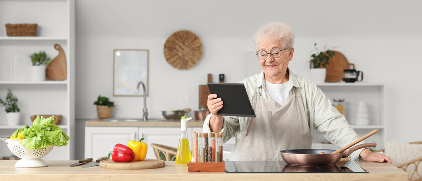 Senior woman with tablet computer frying vegetables in kitchen