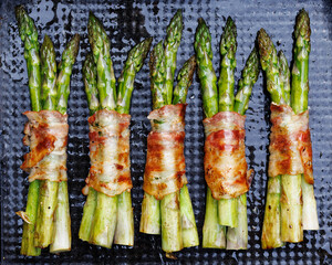 Grilling green asparagus wrapped in bacon on a dark background, top view