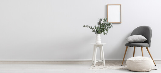 Chair and vase with eucalyptus twigs on stool near white wall in room. Banner for design