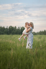 A woman lifts and kisses her daughter in the air while they are having fun together in nature. The concept of lifestyle, family, playing with children
