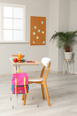 Modern school desk with backpack, lunch and stationery in room near white wall