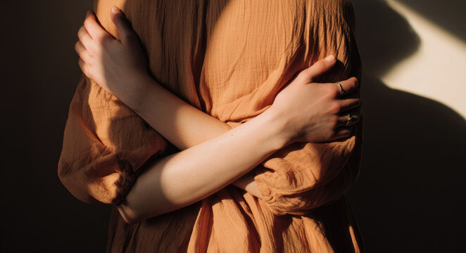 Person in soft, textured fabric embraces themselves, casting gentle shadow. warm lighting creates serene and introspective mood
