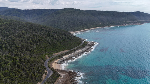 Aerial of road bending along mountains by the ocean