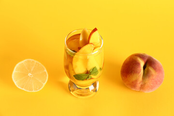 Glass of fresh peach lemonade with mint on yellow background