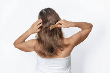 Woman with bare shoulders in a white towel combing her medium length hair. Concept of care and...