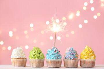 Tasty birthday cupcakes with sparkler on color background