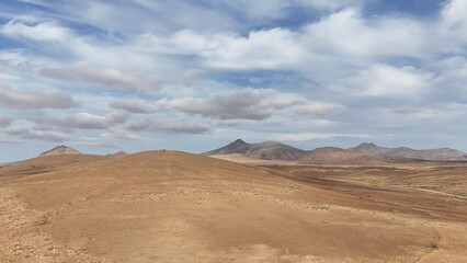 Desert landscape with dry vegetation, mountains in the background, and a wide sky