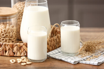 Glasses and jug of fresh milk with cereal rings on wooden table