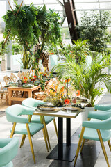 Wedding table setup with zoo floral arrangement. Stylish Dining Table in Greenhouse. Tropical Table Setting with Flowers. A stylish dining table set in a greenhouse, surrounded by lush green plants.