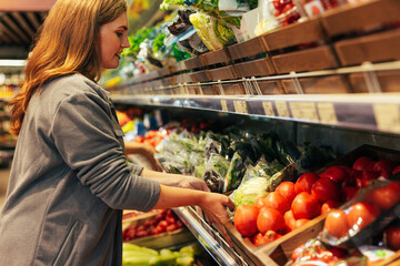 Female grocery store worker refreshing products on the shelf, moving a box