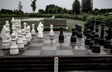 An expansive outdoor chessboard with oversized white and black chess pieces set up on a checkered...