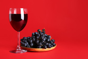 Glass of wine with grapes on red background
