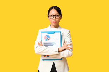 Portrait of young Asian businesswoman with charts on yellow background