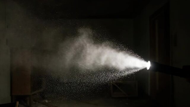 Water spray from a fire extinguisher in dark room with dust particles  