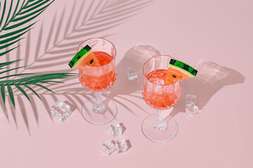 Summer scene with refreshing watermelon drink and palm tree leaves shadow on pink and white background. Sun and shadows. Minimal cocktail concept. Trendy summertime party idea. Summer aesthetic.