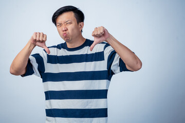 Asian man in striped shirt making a double thumbs-down gesture with a displeased facial expression,...