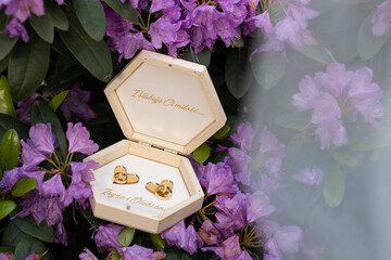 Wedding wooden box with purple flowers, covered with white tulle. Gold rings in an unusual wooden...