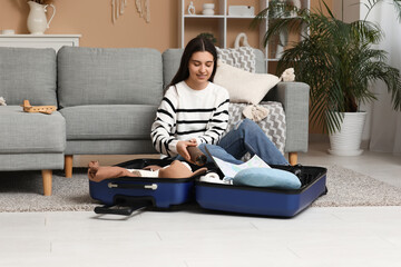Obraz premium Young woman packing suitcase on floor at home. Travel concept