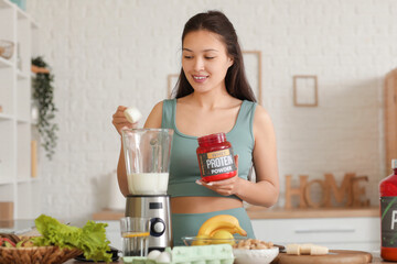 Sporty young happy Asian woman making protein shake at home