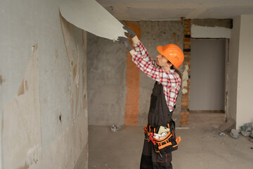 Builder worker peeling off wallpaper during interior home renovation. vertical view.