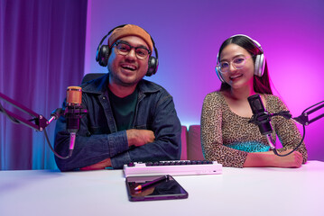 Two young asian streamer host making live podcast with condenser microphone and tablet at broadcast...