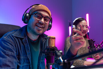 Two young asian streamer host making live podcast with condenser microphone and tablet at broadcast...