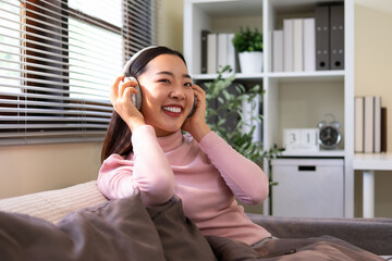 A young woman listens to music through headphones. She is sitting on the sofa.