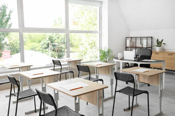 Desks with papers and chairs in empty classroom at school