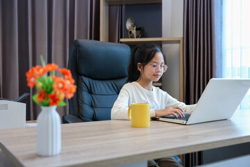 Young asian schoolgirl is doing her class homework assignment at home using laptop computer for education and study concept