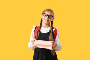 Cute schoolgirl with books and backpack on yellow background