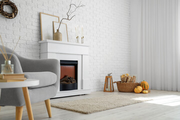 Interior of stylish room with modern fireplace, armchair and autumn decorations near white brick wall