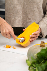 Woman removing Butternut Squash seeds and stringy fibers with a spoon. Vegetable, vegan food