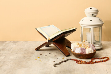 Koran, prayer beads, Turkish delight and lantern on grey table against beige background. Ramadan celebration