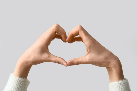 Female hands showing heart gesture on grey background