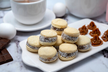Counter with ingredients: eggs, flour, beaters, and cornstarch alfajores with dulce de leche and coconut, chocolate bar with white dishes