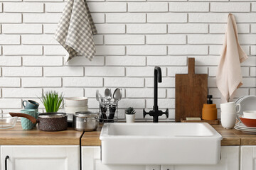 Wooden kitchen counter with sink, clean dishes and towels hanging on light brick wall