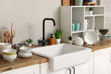 Stylish ceramic sink, clean dishes and shelving unit on wooden kitchen counter