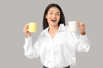 Beautiful young woman with cups of tea on grey background