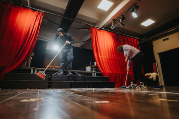 Theatre staff tidying the stage area, surrounded by red curtains and professional lighting,...