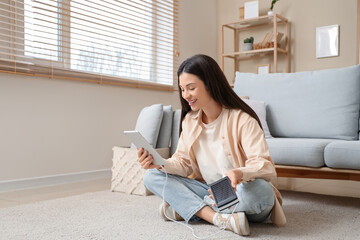 Beautiful young woman with modern power bank using tablet computer at home