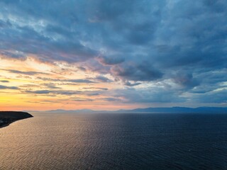 Beautiful cloudy red sunrise over sea with beach, waves and mountains in the background. Impressive structure texture in the sky