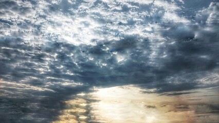 A dramatic cloudy sky with dark, swirling clouds and sunlight piercing through, casting striking...