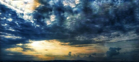 Obraz premium A dramatic cloudy sky with dark, swirling clouds and sunlight piercing through, casting striking beams of light that create a powerful and captivating atmosphere. 