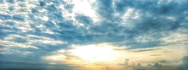 A dramatic cloudy sky with dark, swirling clouds and sunlight piercing through, casting striking beams of light that create a powerful and captivating atmosphere.
