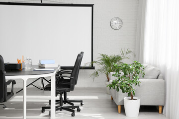 Interior of conference hall with table, sofa, houseplants and projector screen in modern office